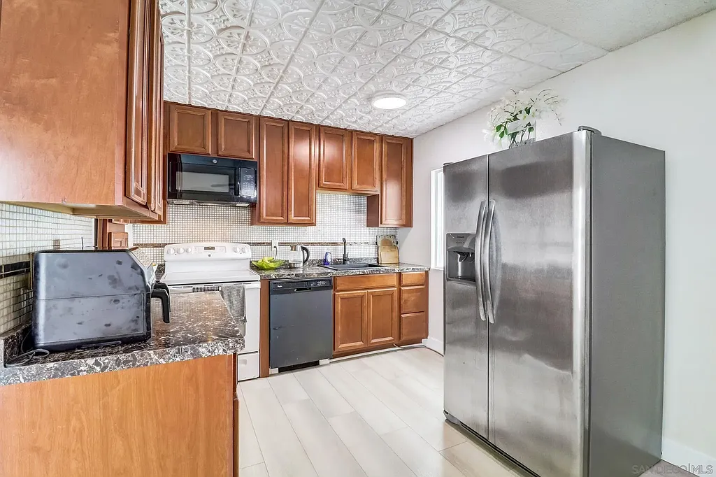 Kitchen in California with stainless steel fridge, dark appliances, wood cabinets, and marble countertops.