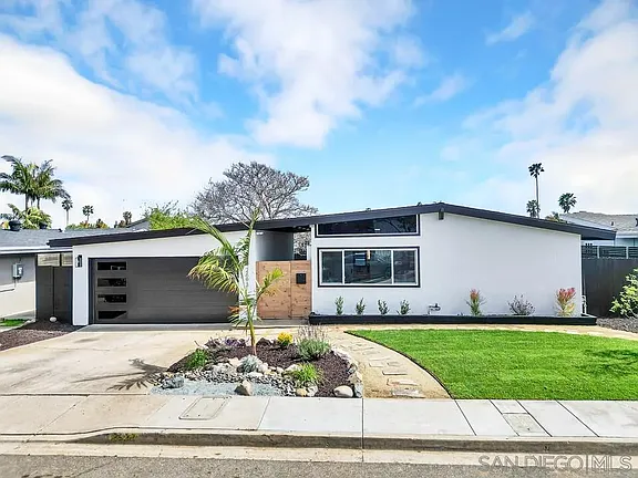 Modern California house with white facade, large window, slanted roof, gray garage door, and landscaped front yard with grass and palm tree.