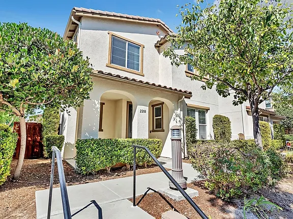 Two-story white house in California with gabled roof, arched porch, and trees.