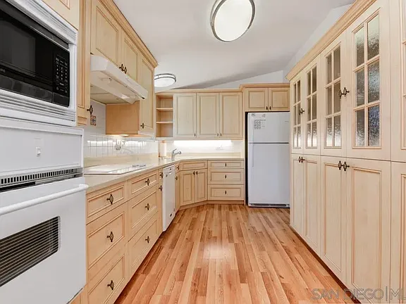 Kitchen in California with wood cabinetry, hardwood floors, white appliances, and glass cabinet doors.