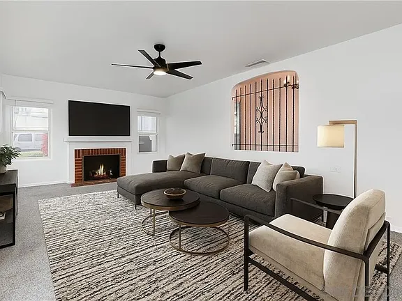 Modern living room in a California house with gray sectional sofa, cream armchair, round coffee tables, fireplace with TV, large rug, and ceiling fan.