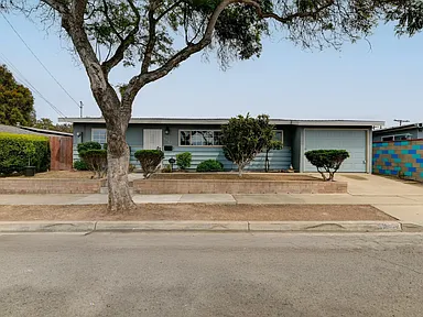 California single-story house with light blue siding, large front tree, driveway, and attached garage.