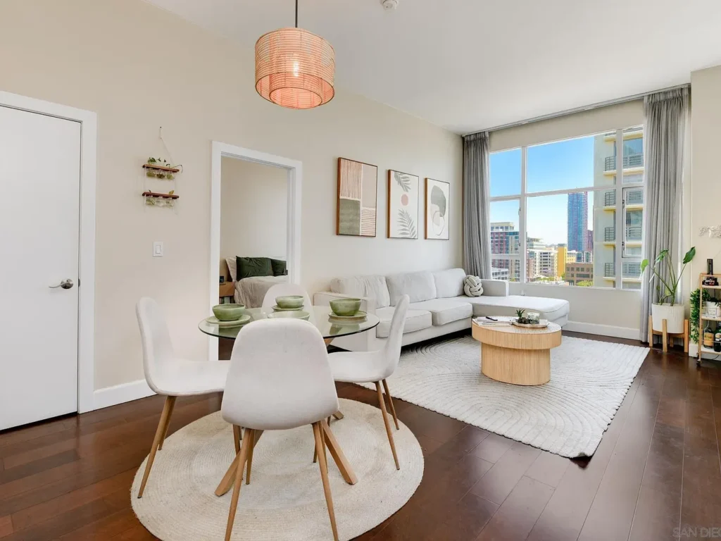 Modern California living room with gray sofa, abstract art, city view, and dining table with plant.